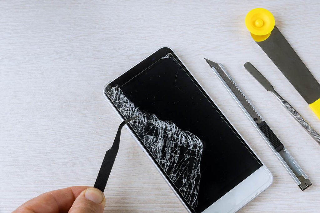 Persona utilizando herramienta sobre teléfono con pantalla rota.
